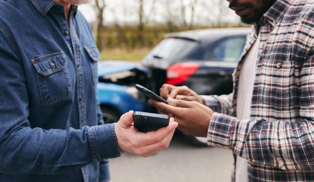 Younger and older drivers at side of the road exchanging car insurance details after traffic accident using mobile phones